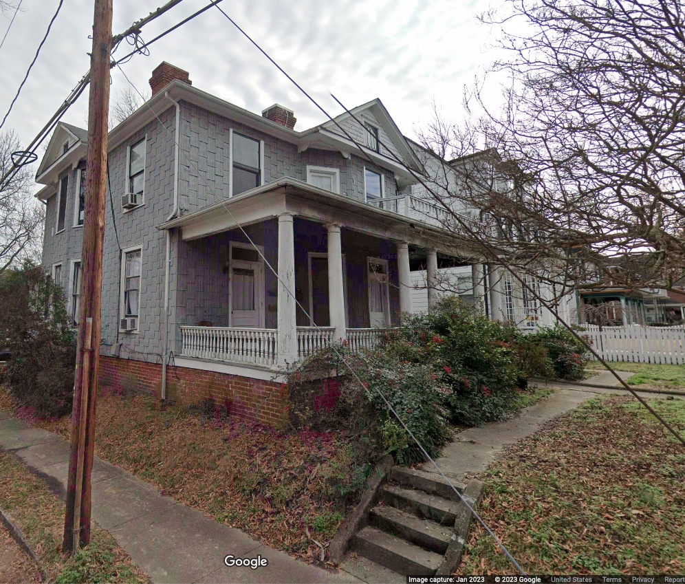 two-story house on a corner with gray asbestos-shingle siding